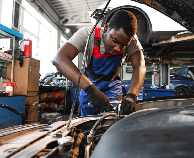 Young African male mechanic repairs car in garage close up Young African male mechanic in uniform repairs car in garage close up