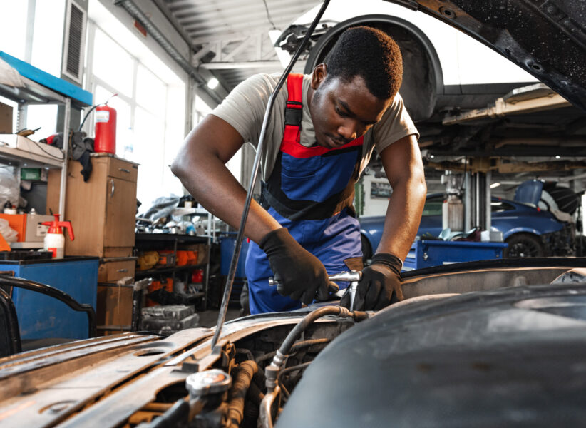 Young African male mechanic in uniform repairs car in garage close up