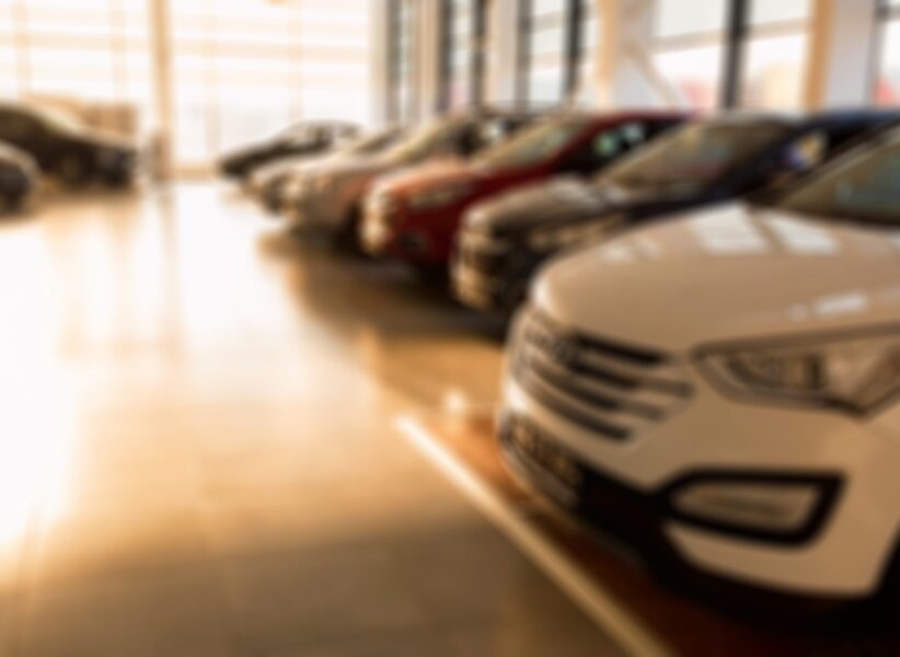 Stock of cars in showroom of automobile dealer with sunlight from window. Blurred
